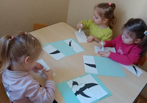Dzieci przyklejają pociętą ilustracje jaskółki na kartkę papieru