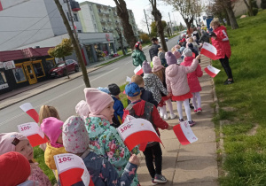 dzieci maszerują ulicami miasta z flagą Polski