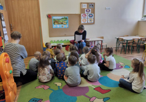 Dzieci słuchają uważnie zagadek czytanych przez nauczycielkę