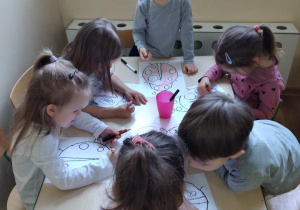Dzieci wykonują pracę grafomotoryczną - rysują po śladzie biedronkę, wypełniają kredkami kontury obrazka