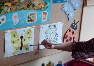 Nauczycielka tłumaczy dzieciom jak wykonać pracę z użyciem farb