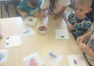 dzieci siedzą przy stoliku, dzieci układają koraliki według szablonów