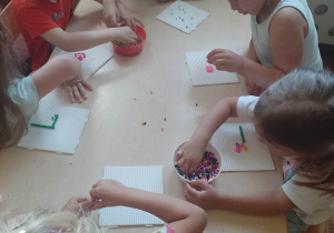 Dzieci przy stolikach z plastikowych koralików tworzą wakacyjny obrazek