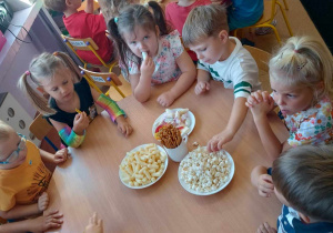 Dzieci z grupy Pszczółek świętują Dzień Przedszkolaka przy stoliku pełnym słodkich i słonych przekąsek