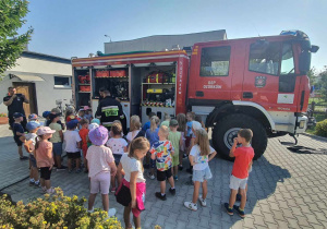 Dzieci z zainteresowaniem oglądają wóz strażacki i jego wyposażenie