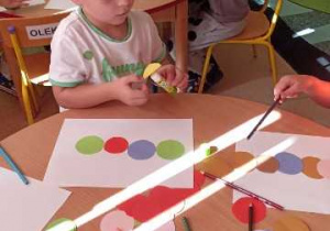 Dzieci przyklejają kolorowe koła tworząc gąsienicę