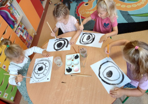 Dziewczynki przy stoliku malują obraz z wykorzystaniem czarnych kół i kropek