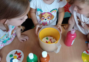 Dziewczynki z zainteresowaniem przyglądają się talerzykowi z kolorową farbą umieszczonemu w wirówce