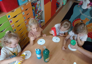 Dzieci wylewają po kropelce kolorowe farby na papierowy talerzyk