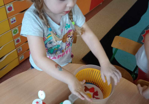Dziewczynka ostrożnie umieszcza papierowy talerz z kroplami farb w wirówce