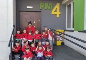 Dziec iz Panią pozują do zdjęciaw czerwonych koszulkach w kropki, kucając na schodach w wejściu do przedszkola.