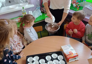 Nauczycielka wraz z dziećmi z pomocą miksera szykuje ciasto na świąteczne babeczki