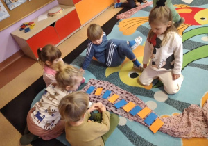 Dzieci w grupach układają prostokąty na szalu według określonego rytmu