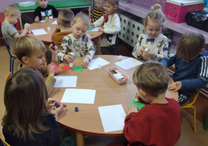 Dzieci przyklejają na kartkę wylosowane wcześniej figury geometryczne z kolorowego papieru