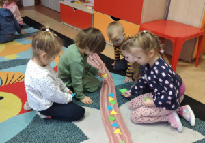 Dzieci w grupach układają trójkąty na szalu według określonego rytmu