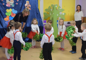 Nauczycielka wraz z dziećmi wykonuje układ taneczny z pomponami dla dziadków