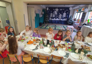 dzieci siedzą przy stole i jedzą