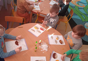 Dzieci wykonują przy stolikach pracę plastyczną - dekorują pączki różnymi materiałami plastycznymi
