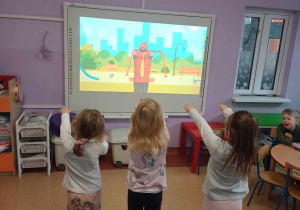 Chętne dzieci wykonują ćwiczenia ruchowe przed tablicą multimedialną