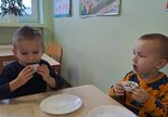 Dwaj chłopcy jedza babeczki przy stoliku na talerzykach.