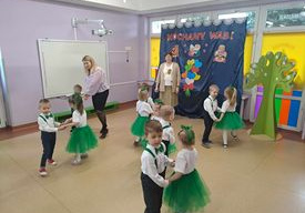 Dzieci tańcza w parach pięknie ubrane na udekorowanej sali.