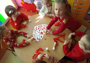 Dzieci wspólnie przy stoliku ozdabiają serce kulkami z czerwonej bibuły