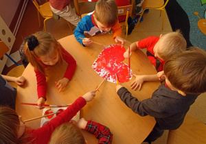 Dzieci wspólnie przy stoliku malują serce farbami przy użyciu pędzli
