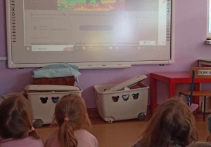 Dzieci oglądają film edukacyjny na tablicy multimedialnej - poznają różne gatunki dinozaurów