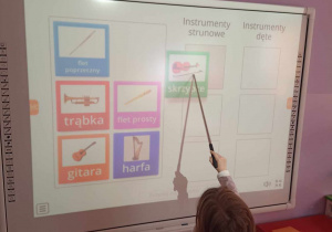 Dziewczynka w prawidłowy sposób segreguje instrumenty na tablicy multimedialnej dzieląc je na dęte i strunowe