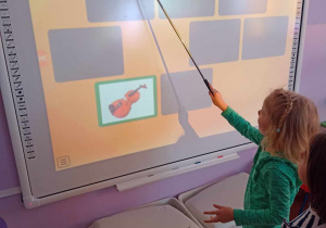 Dziewczynka rozpoznaje instrument na tablicy multimedialnej i szuka drugiego takiego samego obrazka