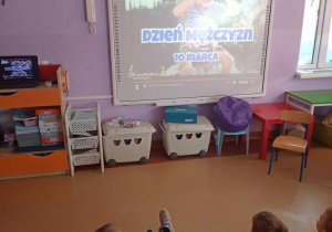 Dzieci oglądają na tablicy multimedialnej film edukacyjny o Dniu Mężczyzn
