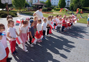 Dzieci szykują zbierają się w ogrodzie przedszkolnym aby wspólnie zaśpiewać hymn "Mazurek Dąbrowskiego"