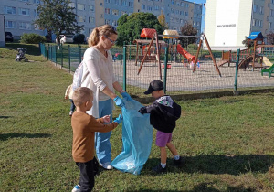 Dzieci wrzucają do niebieskiego worka znalezione przy placu zabaw kartki papieru i ulutki