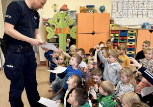 Pan policjant wręcza dzieciom kolorowanki