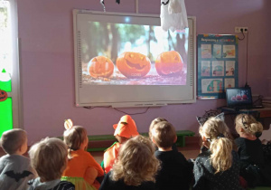 Dzieci oglądają film edukacyjny na tablicy multimedialnej dotyczący ozdabiania dyni na Halloween