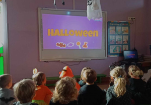 Dzieci oglądają film edukacyjny na tablicy multimedialnej o zwyczajach Halooween