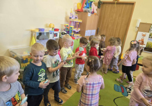 Dziewczynki podchodzą do stojących w szeregu chłopców i wręczają im bezowe kwiatki.