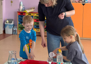 Dziewczynka wlewa ocet do szklanego pojemnika z wodą