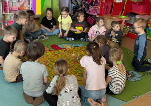 Dzieci w kole obserwują przedmioty, które wrzucone do miski z wodą toną