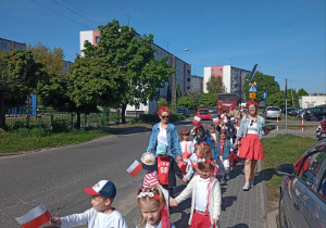Dzieci ubrane na biało czerwono z flagami w reku spacerują wraz z wychowawczyniami ulicami osiedla
